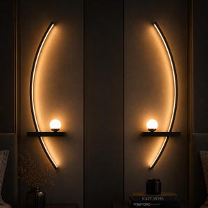 May include: Two wall-mounted light fixtures featuring a curved black frame with integrated warm LED lighting. Each fixture includes a horizontal shelf supporting a small, spherical white glass orb light that emits a soft, glowing illumination.