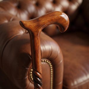Könnte beinhalten: Ein polierter Gehstock aus Holz mit einem glatten, geschwungenen Griff und einem markanten, spiralförmig gedrehten Schaft. Das Holz zeigt eine reiche, warmbraune Maserung mit einer glänzenden Oberfläche, die die natürliche Textur betont.