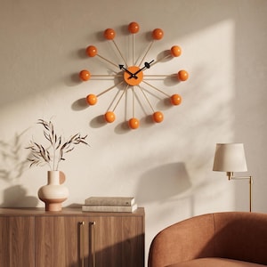 May include: A sunburst wall clock featuring a central orange circular face with black hands and twelve thin metal spokes extending outward, each tipped with a smooth orange sphere. The design radiates from the center in a starburst pattern.