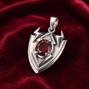 May include: A silver-toned metal pendant shaped like a shield with a pointed base and two lightning bolt motifs at the top. A round, deep red gemstone is set in the center of the shield, held by four prongs. A metal bail is attached to the top.