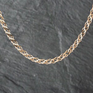 May include: A gold chain necklace featuring a woven, interlocking link design. The chain is composed of polished, reflective metal links that create a continuous, braided pattern throughout the length of the jewelry piece.
