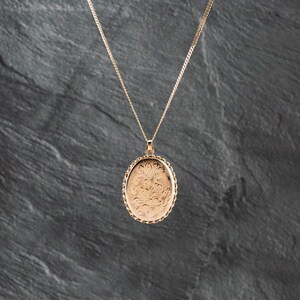 May include: A rose gold-toned oval locket pendant suspended from a matching delicate chain. The locket features an intricate floral engraving on its front surface and is framed by a decorative beaded edge, creating a classic jewelry piece.