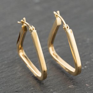 May include: A pair of gold hoop earrings with a distinct triangular shape. Each earring features a smooth, polished metallic surface and a hinged post mechanism at the top, allowing the hoop to open and close securely for comfortable wear.