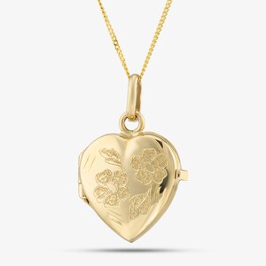 May include: A gold heart-shaped locket pendant suspended from a delicate gold chain. The front surface of the locket features a polished finish with two etched floral designs that have a textured, matte appearance, including leaves and petals.