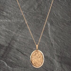 May include: A rose gold-toned oval locket pendant suspended from a delicate matching chain. The locket features an intricate, engraved floral pattern across its front surface, showcasing detailed leaf and petal motifs in a polished metal finish.