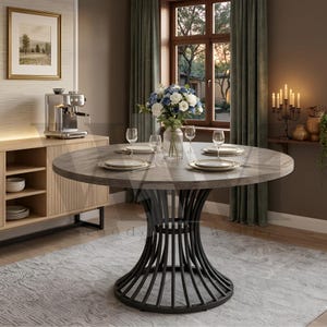 May include: A round dining table with a grey wood grain top and a black metal base featuring vertical curved slats. The table is set with four white plates, four clear glasses, and a glass vase containing a bouquet of blue and white flowers.
