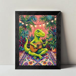 May include: A framed art print featuring a bright green dinosaur sitting on a patterned rug while playing a brown acoustic guitar. The scene is set against a pink background with lush tropical plants and a string of glowing white fairy lights.