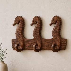 Könnte beinhalten: Eine wandmontierte Garderobe aus Holz mit drei geschnitzten Seepferdchen-Figuren. Jedes Seepferdchen ist nach links ausgerichtet, wobei sich der Schwanz nach oben zu einem Haken krümmt. Das Stück ist aus dunkelbraunem Holz mit sichtbarer Maserung.