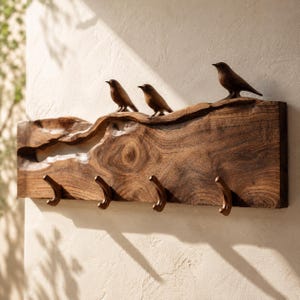 May include: A rectangular wall-mounted coat rack crafted from a single piece of dark brown natural wood with a live edge top. Three small carved wooden bird figures are perched along the top edge, and four matching wooden hooks are attached.