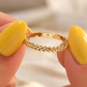 Könnte beinhalten: Ein dünner Goldring mit einem durchgehenden Blatt- oder Rankenmuster um die Ringschiene. Auf der Innenseite des Rings ist deutlich der Schriftzug 14K eingraviert, der den Goldgehalt angibt. Der Ring hat eine polierte Oberfläche.
