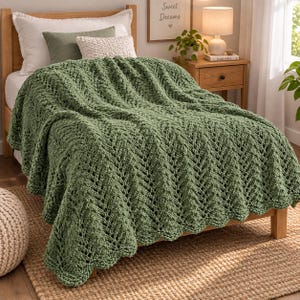 May include: A sage green chunky knit throw blanket featuring a prominent chevron or herringbone stitch pattern. The blanket is draped over a bed, showcasing its thick, textured yarn construction and consistent vertical zig-zag design throughout.