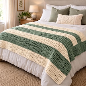 Puede incluir: Una manta de ganchillo gruesa con rayas horizontales alternas en verde bosque y crema. El hilo texturizado crea un patrón de puntos gruesos y elevados en toda la manta rectangular, que está colocada sobre una cama con sábanas blancas.