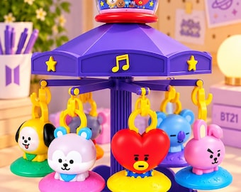 Puede incluir: Un juguete de carrusel morado con personajes BT21. La parte superior tiene una cúpula transparente con figuras en miniatura. Cinco dijes colgantes en amarillo, morado claro, rojo, azul y rosa giran alrededor de un pilar central sobre una base festoneada.