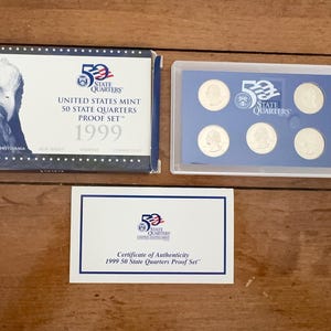 May include: A 1999 United States Mint 50 State Quarters Proof Set including a blue and white cardboard sleeve with an eagle image, a clear plastic case containing five silver-coloured quarters, and a white Certificate of Authenticity card.