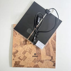 May include: A square 14W heating mat with a black surface and a black power cord featuring an inline switch. The mat is layered over a square cork board with a natural mottled texture and the brand name Repti-Zoo printed in the center.