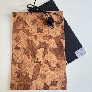 Peut inclure: Un tapis chauffant rectangulaire pour reptile avec une surface texturée en liège dans des tons marron et beige. Le tapis comprend un cordon d'alimentation noir avec un interrupteur et une face inférieure noire avec une étiquette de sécurité.