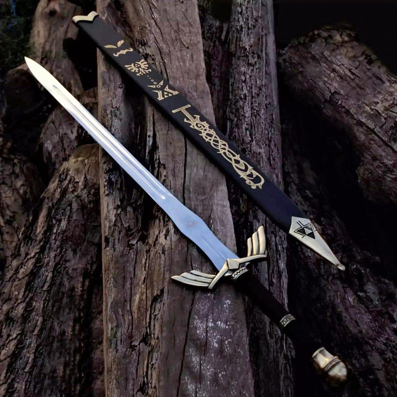 May include: A silver-toned metal sword with a black handle and a gold-colored crossguard featuring wing-like extensions. The matching black scabbard displays gold-colored intricate engravings and a triangular emblem at the pointed tip.