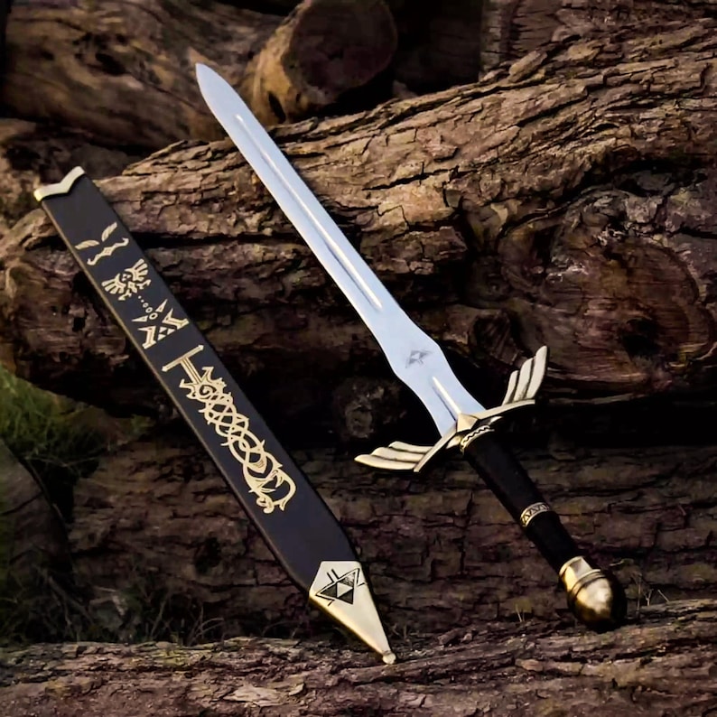 May include: A silver-toned metal sword with a black handle, a gold-colored crossguard featuring wing-like extensions, and a spherical pommel. Beside it lies a black scabbard decorated with gold-colored intricate patterns and a triangular emblem.