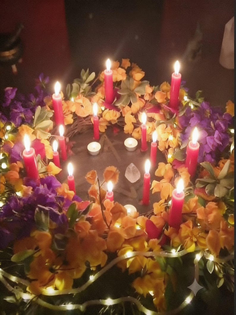 May include: A circular wreath decorated with purple and yellow flowers, green foliage, and small white string lights. Multiple red taper candles and two small white tea light candles are arranged around a central pentagram symbol and a clear crystal.