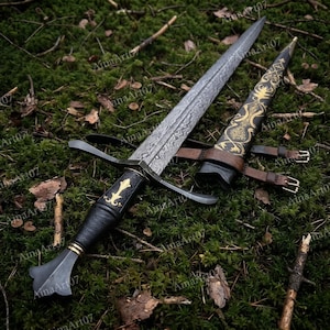 May include: A double-edged dagger with a patterned Damascus steel blade, a black leather-wrapped handle with gold-colored accents, and a matching black scabbard featuring intricate gold-colored filigree patterns and brown leather straps.