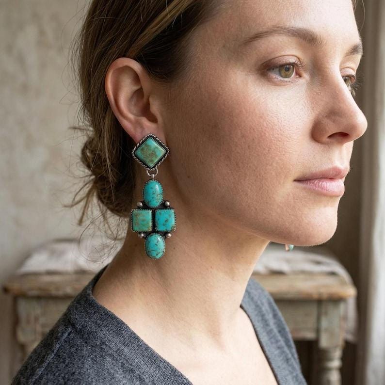 May include: Turquoise and silver earrings. The earrings feature a diamond-shaped top stone, followed by an oval stone, two square stones, and a final oval stone. The stones are a vibrant turquoise color, set in silver metal.