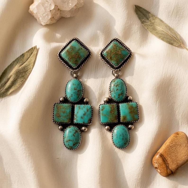 May include: A pair of turquoise and silver earrings. Each earring features a square turquoise stone at the top, followed by an oval stone, two square stones, and another oval stone. The earrings have a silver frame with a twisted rope design.