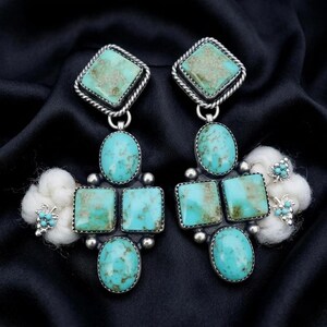 May include: Pair of turquoise and silver earrings. Each earring features a square top stone, an oval stone, two square stones, and a bottom oval stone. The earrings are accented with white cotton-like flowers and small turquoise stones.
