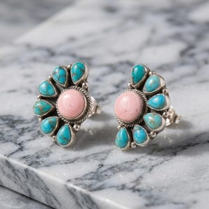 May include: A pair of stud earrings featuring a central round pink stone surrounded by a fan-shaped arrangement of seven teardrop-shaped turquoise stones. The stones are set in silver metal with a twisted rope detail around the center stone.