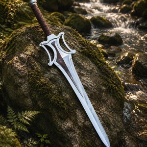 May include: A double-edged sword with a polished silver metal blade, a dark brown leather-wrapped handle, and a decorative silver crossguard featuring a central dark brown inlay that extends down the centre of the blade towards the pointed tip.