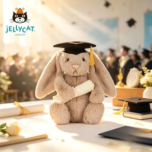 Puede incluir: Un conejito de peluche con birrete negro y borla dorada, sosteniendo un diploma enrollado. El conejito es de color marr&oacute;n claro con orejas largas. El logotipo de Jellycat London es visible. El fondo muestra una ceremonia de graduaci&oacute;n.