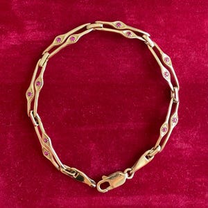Puede incluir: Una pulsera de oro con un diseño de cadena de doble eslabón que presenta pequeñas piedras preciosas redondas de color rosa vibrante engastadas en los eslabones metálicos a intervalos regulares. Incluye un cierre de mosquetón seguro.