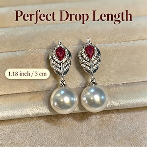 Könnte beinhalten: Ohrringe mit Tropfenform, unten eine perlmuttweiße Perle und oben ein blattförmiges Element mit einem roten Edelstein. Die Ohrringe sind 3 cm lang. Der Text "Perfect Drop Length" steht oben.