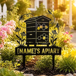 Könnte beinhalten: Schwarzes Metall-Gartenschild mit einer stilisierten Bienenwabe mit Wabenmustern und Bienenmotiven. Das Schild trägt die Aufschrift "[NAME'S APIARY]" und befindet sich in einem Garten mit Blumen und Blättern.