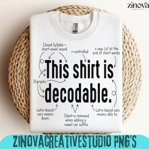 Könnte beinhalten: Ein weißes Sweatshirt mit Rundhalsausschnitt und schwarzem Text, der This shirt is decodable lautet. Das Design enthält verschiedene sprachliche Anmerkungen mit Pfeilen, die auf bestimmte Wörter zeigen und Konzepte wie geschlossene Silben und Digraphen erklären.