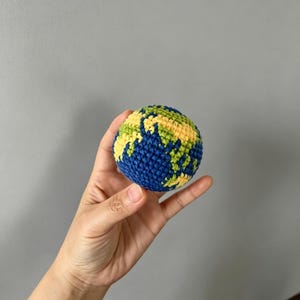 May include: A spherical crochet object designed to resemble the planet Earth, featuring textured yarn in shades of deep blue for the oceans and a combination of bright yellow and green for the landmasses, crafted with a consistent, dense stitch pattern.