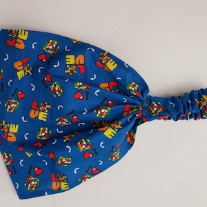 May include: Blue headband with a repeating pattern of colorful Rubik's cubes and the word "LOVE".