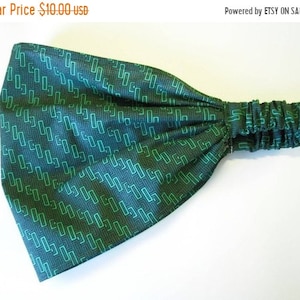 May include: Green and dark gray headband with a geometric pattern. The headband is made of fabric and has a gathered elastic band.