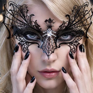 May include: A black filigree masquerade mask featuring an intricate spiderweb pattern and a central bat-like motif. The mask is embellished with clear, sparkling rhinestones arranged along the bridge of the nose and the central design element.