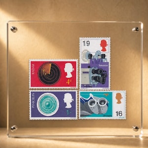 May include: A clear acrylic frame containing four vintage British postage stamps. The stamps feature illustrations of radar, television, penicillin, and a jet engine, each with a silhouette of Queen Elizabeth II and specific denominations.