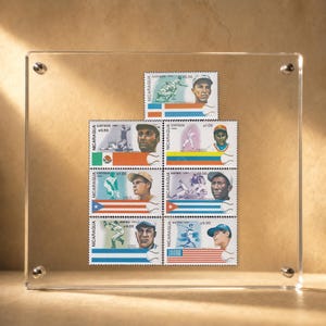 Könnte beinhalten: Eine Sammlung von sieben alten Briefmarken aus Nicaragua mit Baseballspielern und Nationalflaggen, präsentiert in einem transparenten Acrylrahmen mit vier silberfarbenen Metalleckbefestigungen. Jede Briefmarke enthält Text zur Angabe von Land und Wert.