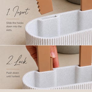 May include: A light gray, oval-shaped container with a ribbed exterior texture and two tan, flat, rectangular hooks. The image displays two steps: 1. Insert, showing the hooks above the slots, and 2. Lock, showing the hooks pushed into the slots.