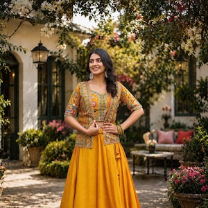May include: A mustard yellow three-piece ensemble consisting of a floor-length skirt, a matching cropped top, and a short-sleeved jacket. The jacket and top feature intricate multi-colored floral embroidery and mirror work detailing throughout.