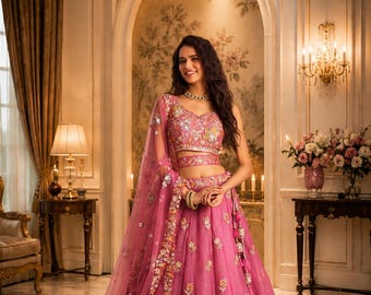 Peut inclure: Un ensemble lehenga rose vif composé d'un haut sans manches et d'une jupe longue volumineuse, richement ornés de broderies florales complexes en argent et or, de sequins et de perles, accompagné d'une dupatta en filet transparent assortie.