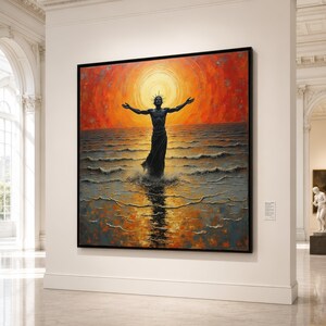 Op de afbeelding: Een groot ingelijst schilderij met een donker silhouet van een figuur die met gespreide armen in de oceaangolven staat. Een heldere, stralende oranje en gele zon gloeit achter de figuur en werpt een glinsterende reflectie over het wateroppervlak.