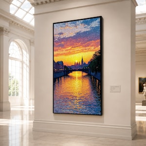 May include: A framed mosaic art piece depicting a sunset over a river with a bridge and city skyline. The sky transitions from blue to orange and yellow, reflecting in the water. The artwork is displayed in a gallery setting.