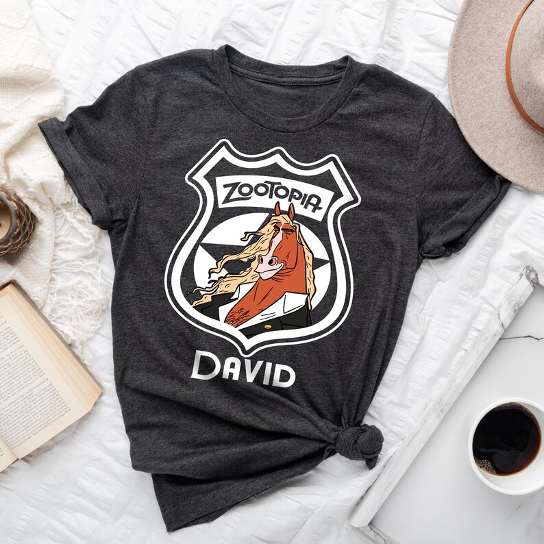 May include: Dark gray t-shirt featuring a Zootopia badge design with a horse character and the name "DAVID" in white. The badge includes the word "Zootopia" in a stylized font. The shirt is knotted at the bottom.