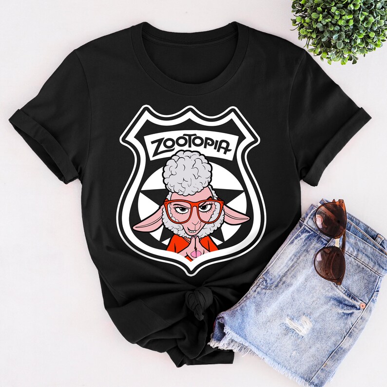 May include: Black t-shirt featuring a graphic from the movie Zootopia. The design includes a sheep character wearing glasses, set within a police badge shape, with the word "Zootopia" at the top. The shirt is made of a soft material.