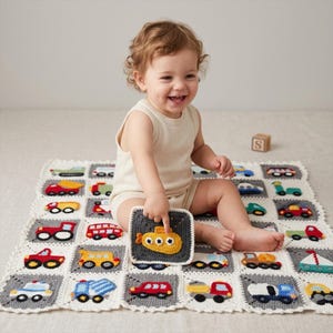 May include: A square crochet blanket featuring a grid of white and gray squares, each decorated with a colorful yarn applique of various vehicles including cars, trucks, and a submarine. The blanket has a scalloped white border edge.