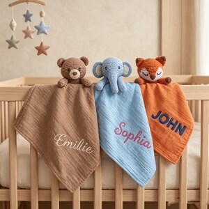 Könnte beinhalten: Drei Baby-Schmusetücher mit gehäkelten Tierköpfen: ein Bär, ein Elefant und ein Fuchs. Jede Decke hat eine andere Farbe: Braun, Blau und Orange. Die Namen "Emilie", "Sophia" und "John" sind auf die Decken gestickt.