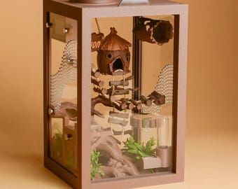 May include: A rectangular brown terrarium enclosure with clear glass panels. Inside, a small brown hut with a thatched roof sits on a branch, connected by a rope ladder to a base with artificial green plants and a clear water dispenser.